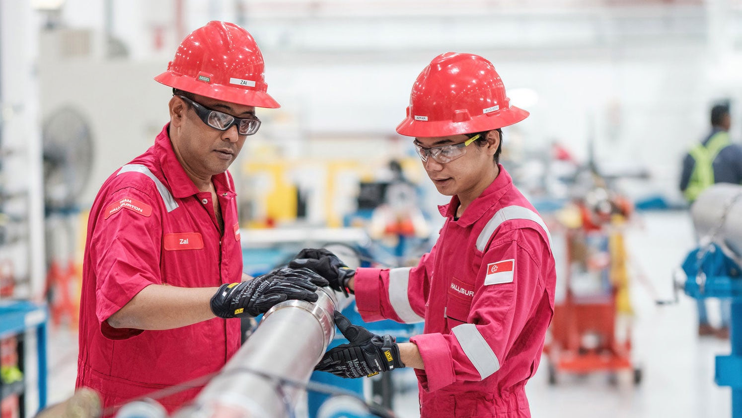Two Halliburton employees in red coveralls working on equipment.